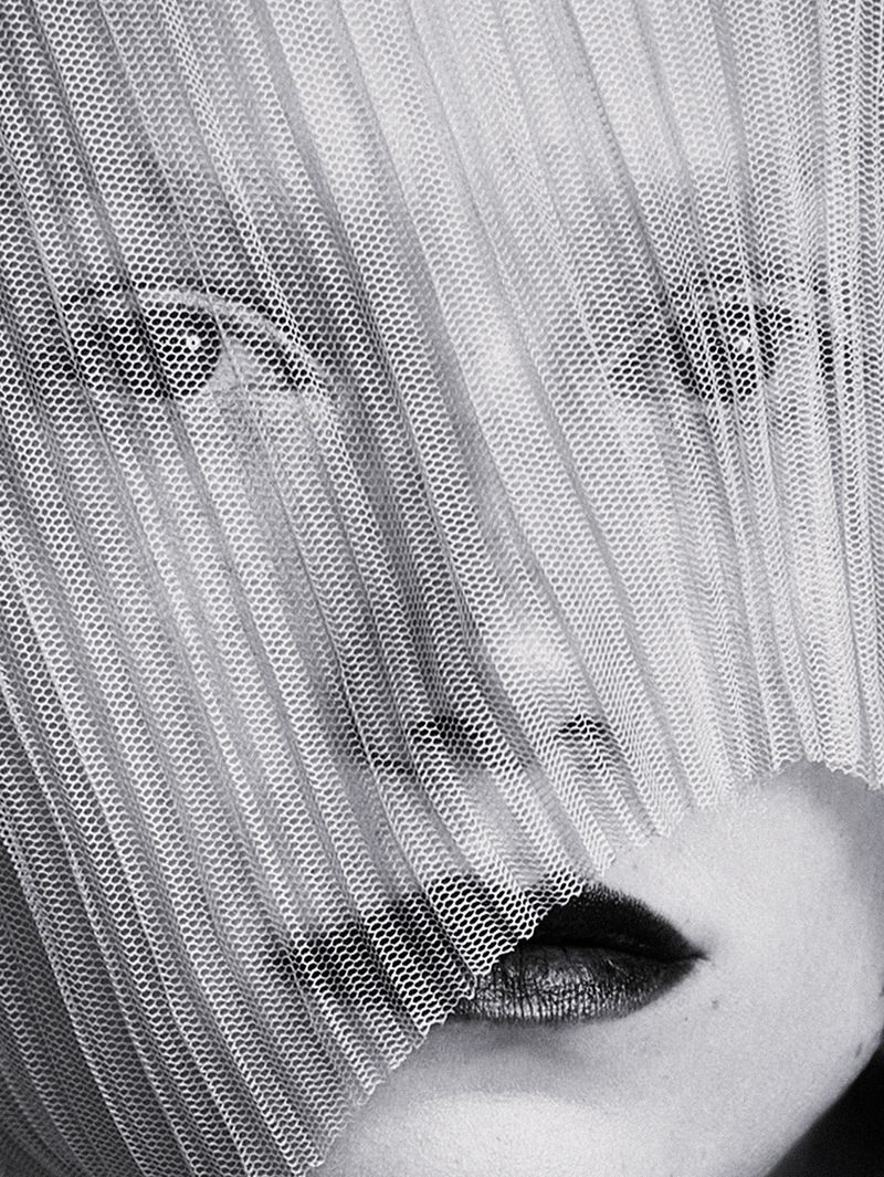 Close-up portrait of a woman's face partially veiled by a textured, semi-transparent fabric, featuring dark lipstick and visible eyes.