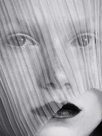 Close-up portrait of a woman's face partially veiled by a textured, semi-transparent fabric, featuring dark lipstick and visible eyes.