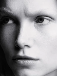 Black and white close-up portrait of a woman looking aside, highlighting natural skin texture, freckles, and light eyebrows.