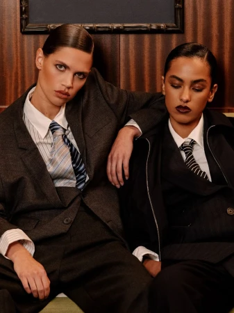 Two women in tailored suits and ties seated against a dark wood paneled interior for Numero Netherlands.