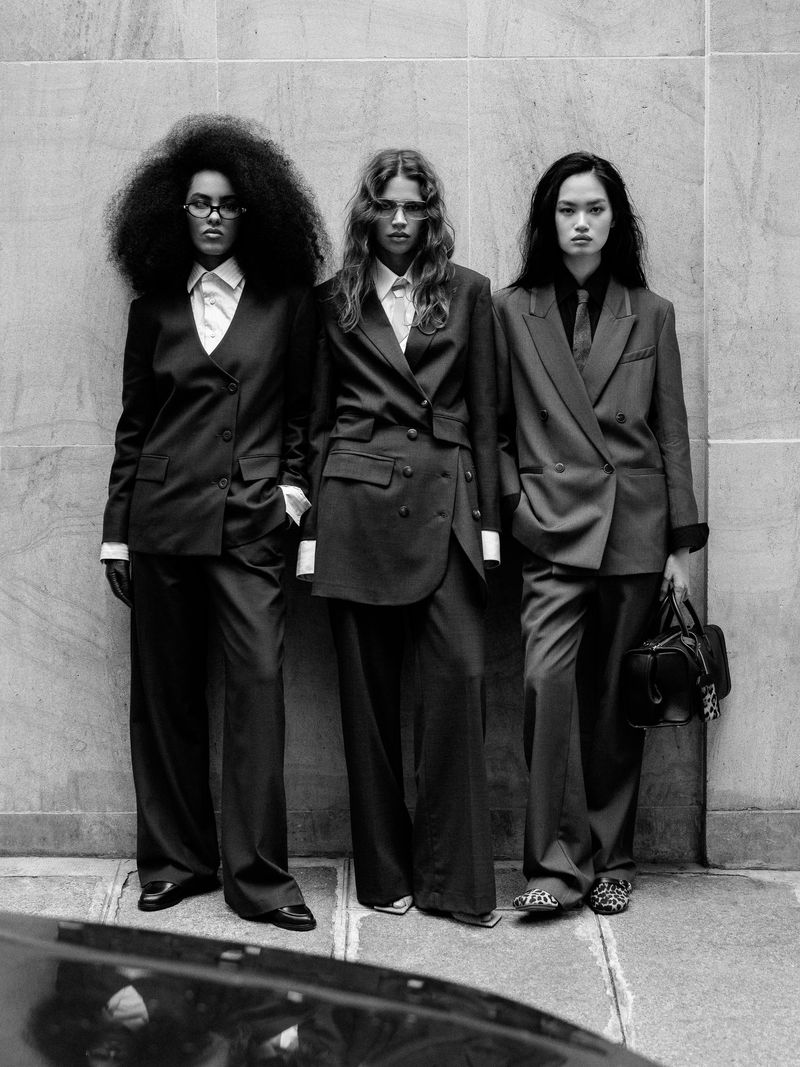 Black and white portrait of three women in oversized suits standing in a row. Fashion editorial showcasing androgynous formal wear.