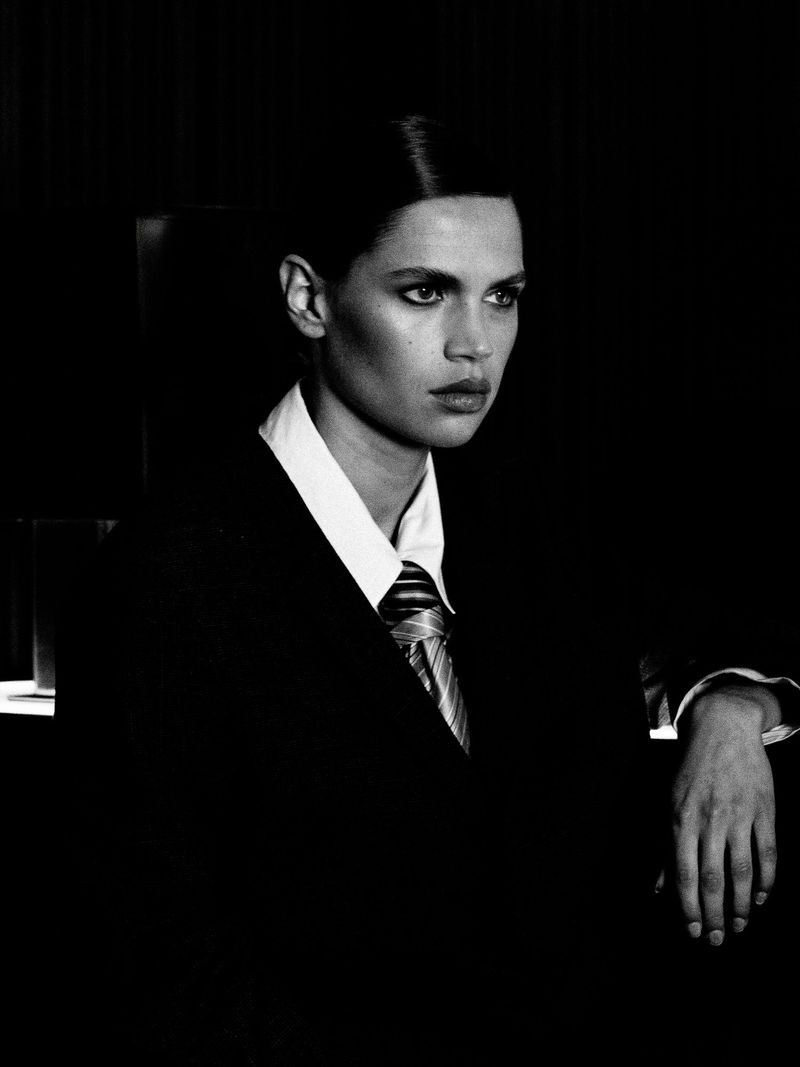 Black and white portrait of a woman in a business suit with a white collared shirt and striped tie looking away from the camera.