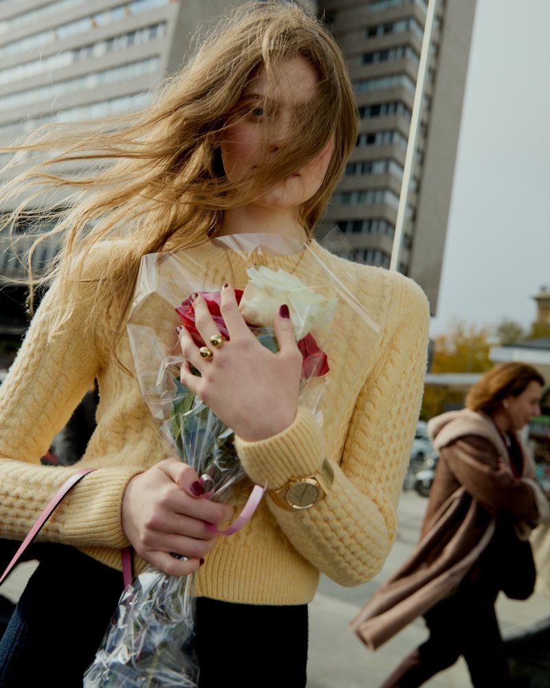 Woman holding a bouquet of red and white roses in an urban setting with a tall building in the background and another woman walking by.
