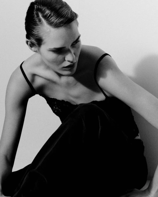 Black and white portrait of a woman with slicked-back hair wearing a camisole, posing in a photo studio.