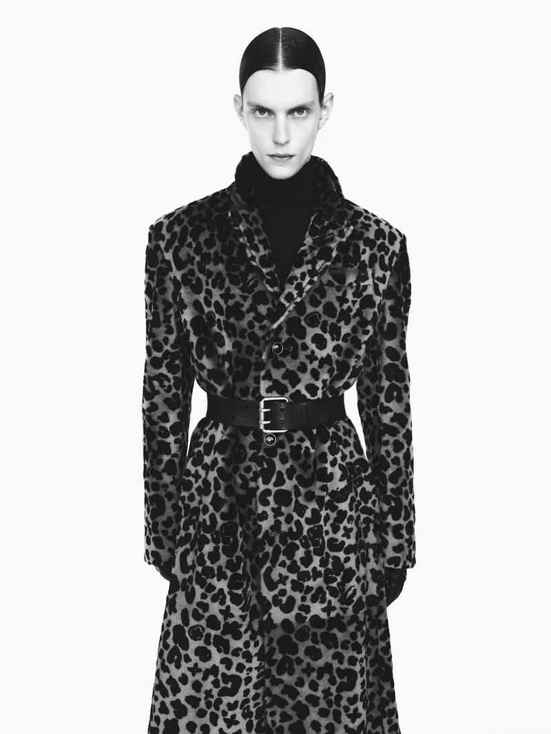 A fashion portrait of a woman in a leopard-print coat with a black belt and gloves, set against a clean white background in a studio.