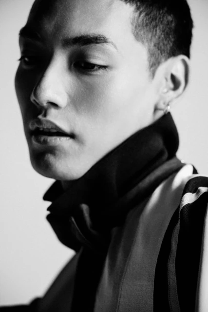 Monochrome portrait of an Asian man with short hair wearing a striped shirt against a grey background, showcasing a modern aesthetic.