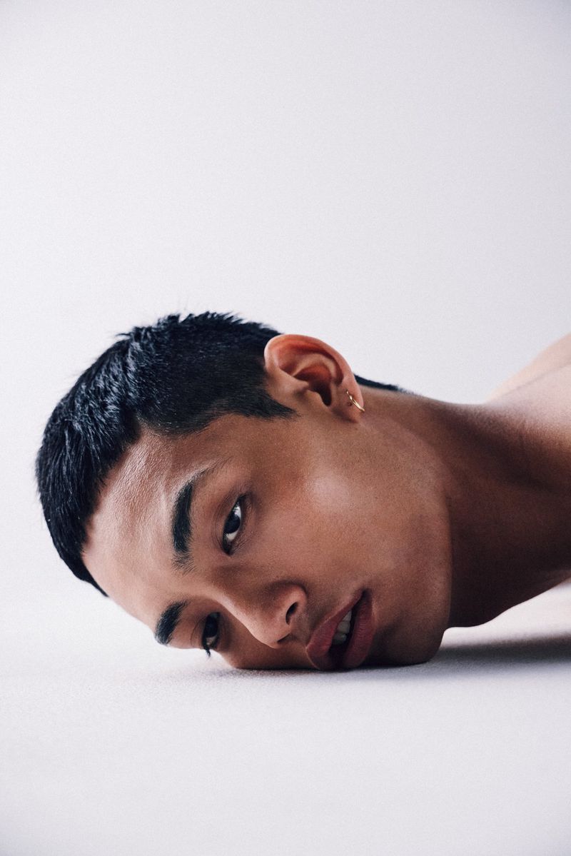 Portrait of an East Asian adult male with short black hair and an earring looking at the camera against a white studio backdrop.