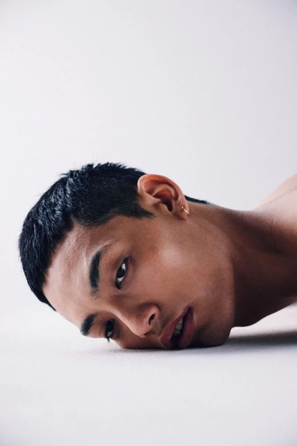 Portrait of an East Asian adult male with short black hair and an earring looking at the camera against a white studio backdrop.
