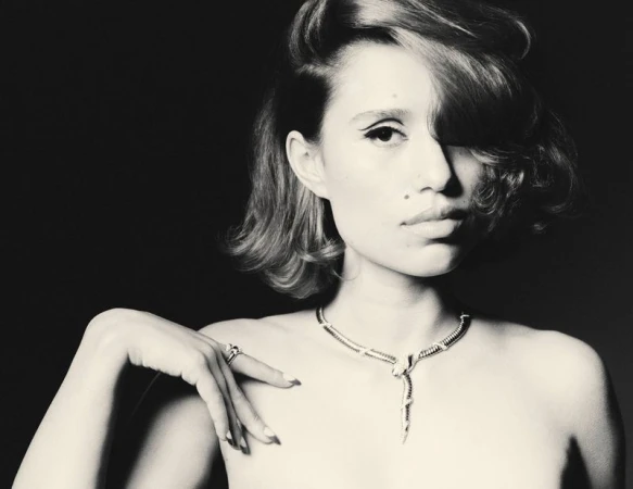 Black-and-white portrait of a young woman wearing a snake necklace and a ring, with dramatic eye makeup and styled short hair.