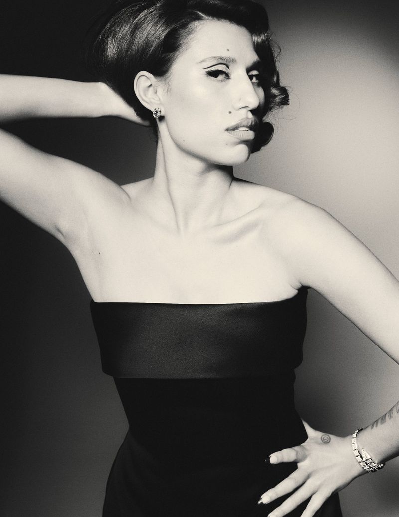 Monochrome studio portrait of a woman with a retro hairstyle and black strapless dress, posing with hand on hip, looking left.