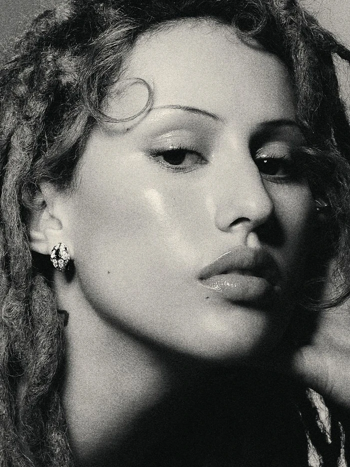 Close-up portrait of Raye wearing diamond earring and textured locs against a plain background for Bulgari.