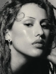 Close-up portrait of Raye wearing diamond earring and textured locs against a plain background for Bulgari.