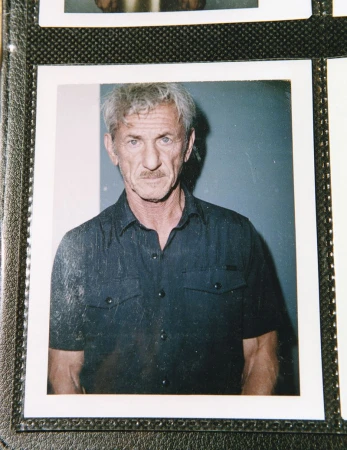 Portrait of an adult man with graying hair and a mustache, wearing a dark blue button-down shirt, captured in a medium studio shot.