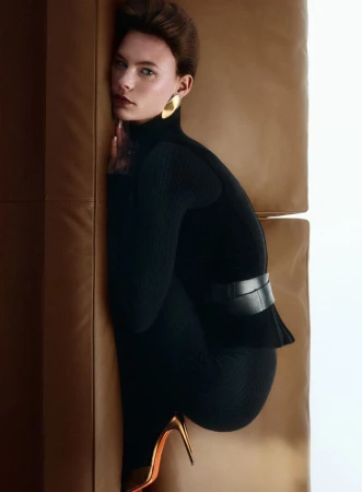 Coline Leclere poses on a tan leather sofa in a black ribbed turtleneck and metallic stiletto heels for Vanity Fair Italia.
