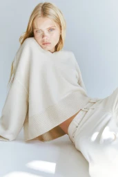 Blonde female model wearing a cream knit sweater against a plain white studio background