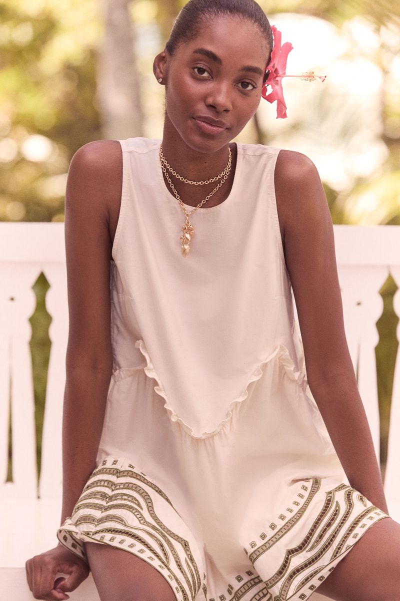 Woman in neutral playsuit with floral hair detail poses outdoors in soft light, showcasing fashion and natural beauty.