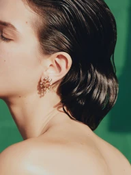 Close-up profile of a model wearing delicate gemstone leaf earrings against a solid green background.