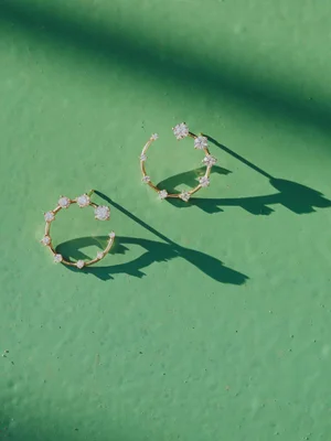 Pair of Fernando Jorge gold open hoop earrings with prong-set diamonds casting sharp shadows on a textured green surface.
