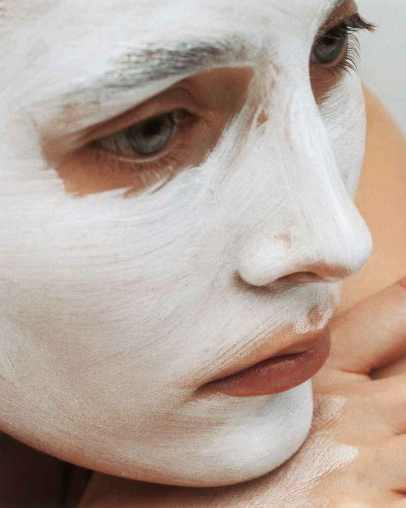 Close-up portrait of a fair-skinned adult female with a white cosmetic face mask treatment, showcasing skincare and beauty.