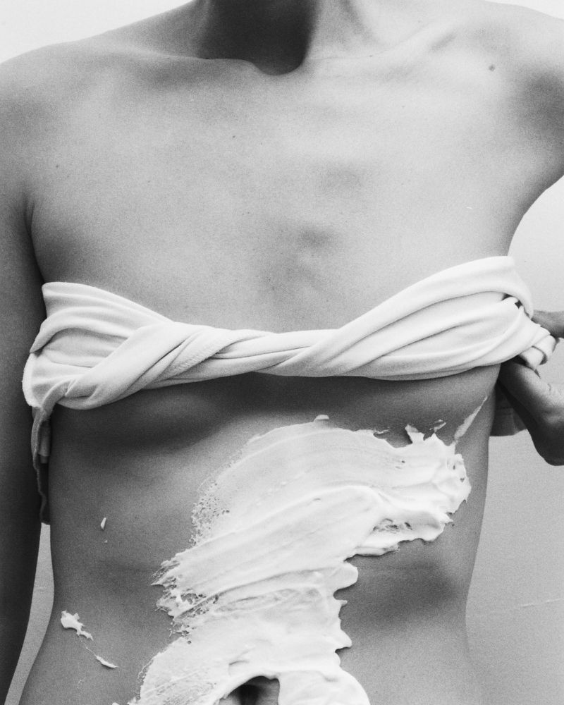 Monochrome close-up shot of a woman's torso partially covered with a draped fabric and white cream or paste.