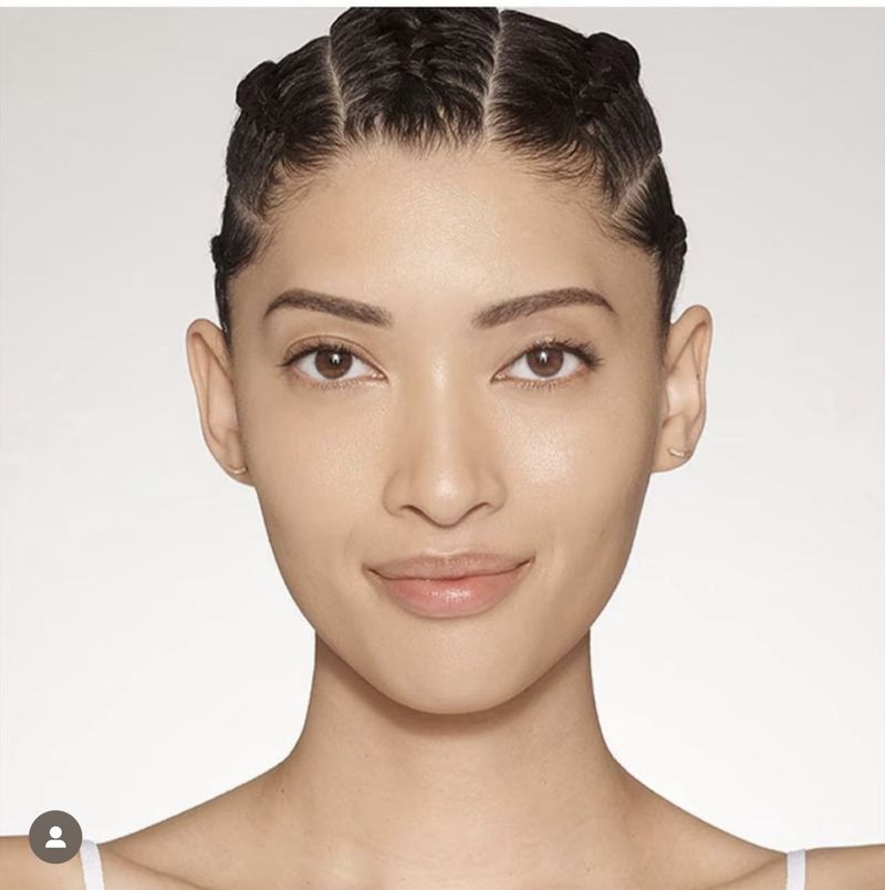 Close-up of a young adult woman with braided hair, light skin, and a neutral expression, showcasing beauty and skincare in a studio.