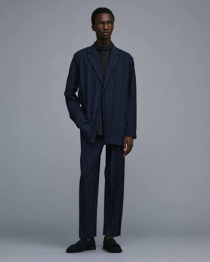 Full-length studio shot of a Black male fashion model wearing a navy suit with a dark grey turtleneck, posing against a grey background.