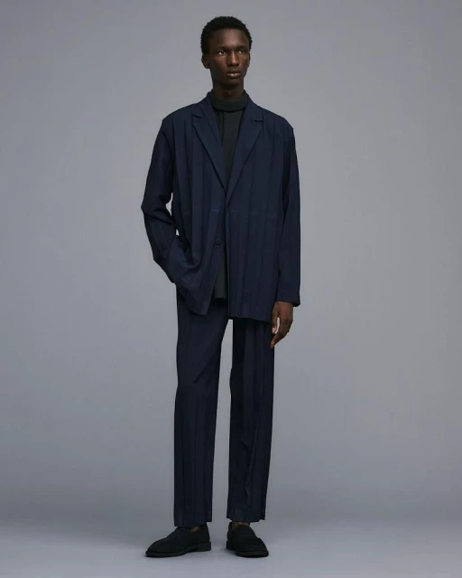 Full-length studio shot of a Black male fashion model wearing a navy suit with a dark grey turtleneck, posing against a grey background.