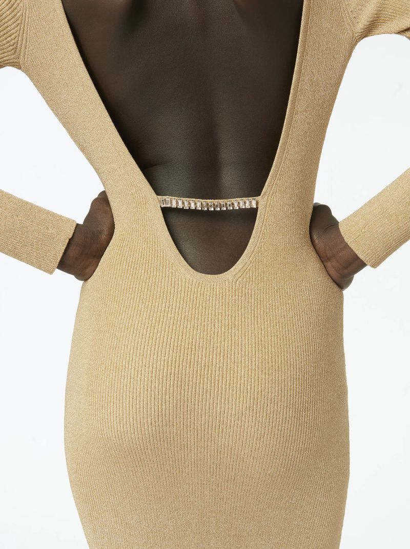 Back view of an adult female in a shiny, tan, ribbed, long-sleeve dress with a deep V-shaped back and decorative gemstone strap detail.