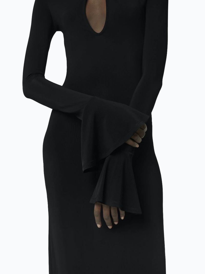 Close-up of a Black adult female wearing a long-sleeved, black, knit midi-dress with bell sleeves against a white background.