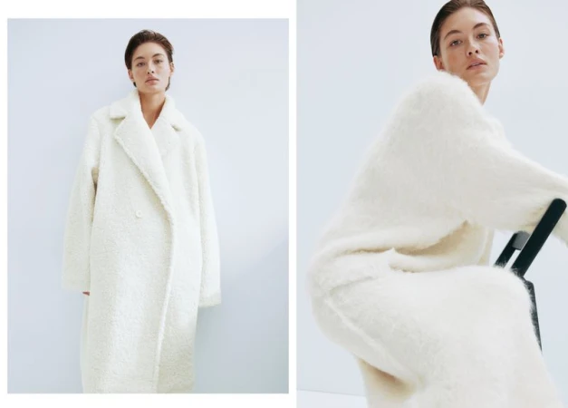 A woman in a white, shaggy coat sits on a black chair against a white background in a studio setting, exuding a minimalist, clean aesthetic.
