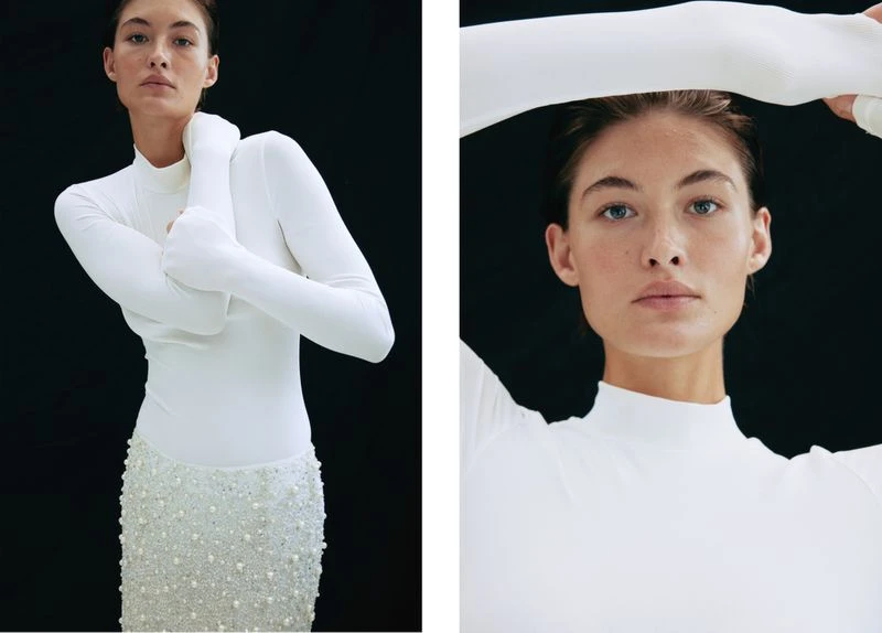 Elegant woman in white long-sleeve top and pearl-embellished skirt against black backdrop, captured in a studio fashion shot with balanced lighting.