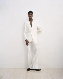 Black man wearing a white suit against a minimalist white studio background