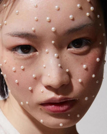 Close-up portrait of a young Asian female model with fair skin adorned with numerous small, round pearls on her face in a beauty context.