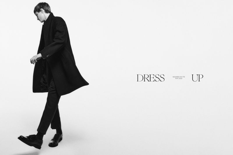 Monochrome studio shot of a male model in a dark coat walking, contrasted against a clean white backdrop with minimalist text overlay.