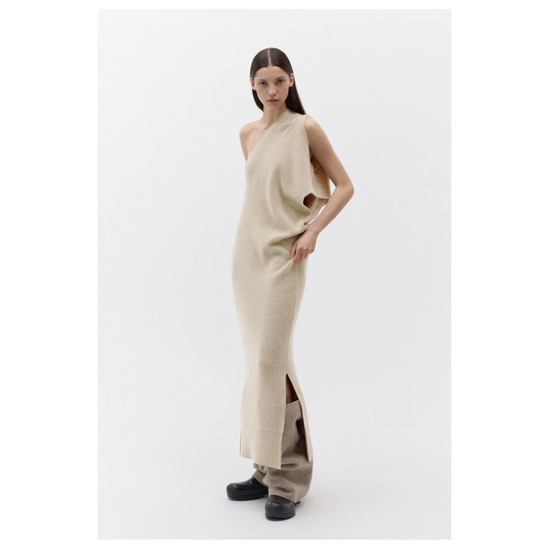 Fashion shot of a solo adult woman wearing a one-shoulder knit dress in a light studio environment with a neutral color palette.