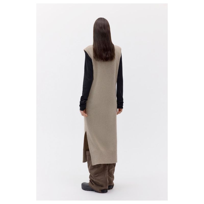 Back view of an adult female wearing a long beige knit dress with high side splits and dark brown boots, set against a neutral backdrop.