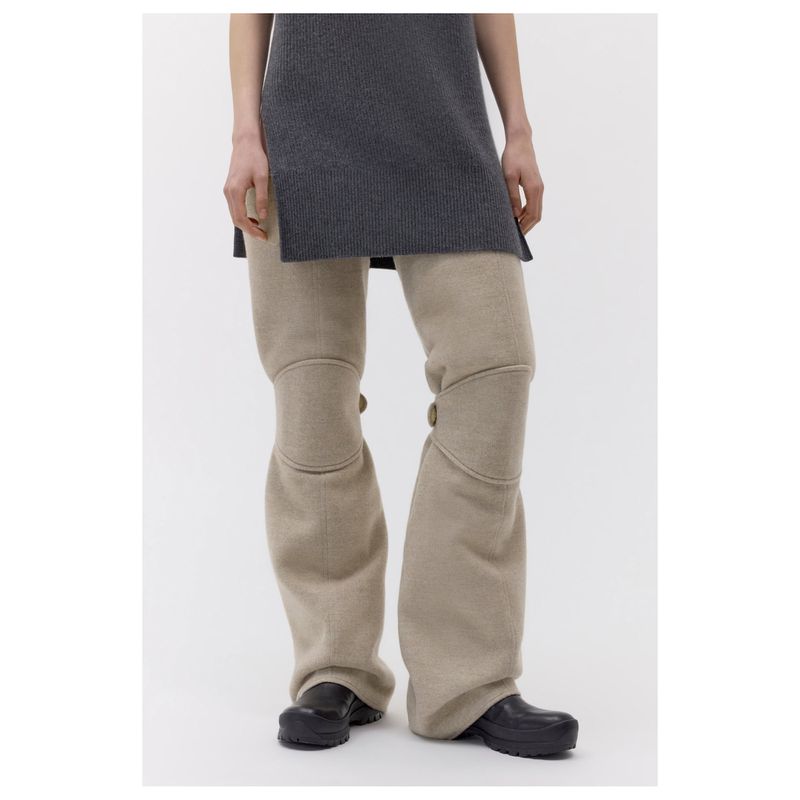Grey knit top paired with tan wool wide-leg trousers and black shoes on a woman in a studio setting on a neutral background.