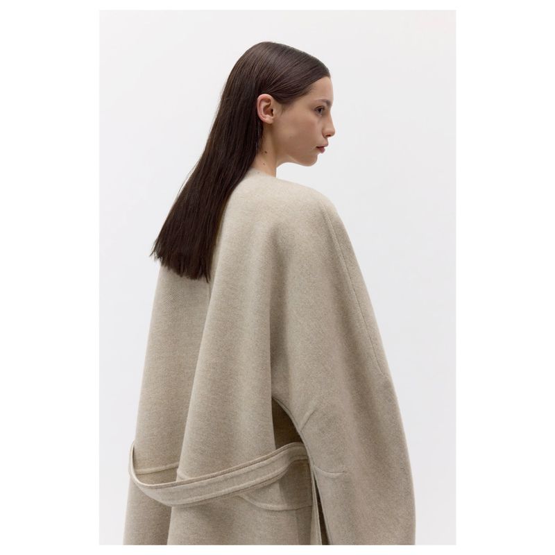 Elegant studio shot of an adult female model wearing a beige wool coat; she poses in profile against a white background.