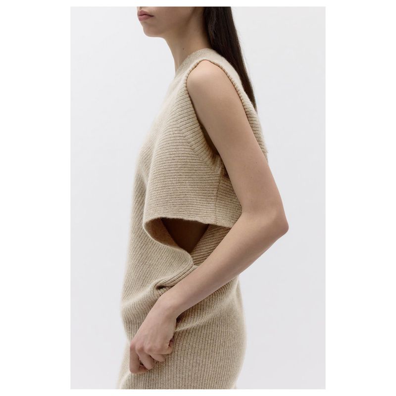 Side view of a woman wearing a beige knit sweater and dress in a brightly lit indoor setting, showcasing fashion and neutral tones.