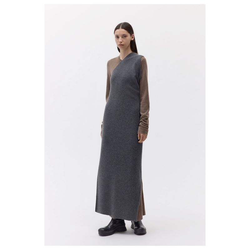Model standing on white studio floor wearing a sleeveless charcoal grey dress over brown long-sleeve top.