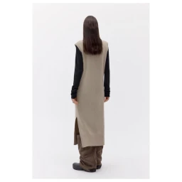 Model seen from behind wearing a long beige sleeveless knit dress over a black long-sleeve top against a white background