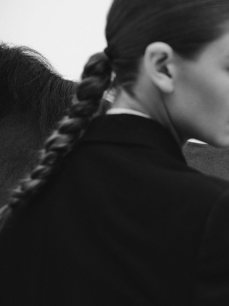 Close-up portrait of a woman with a braided ponytail wearing a dark jacket next to a horse.