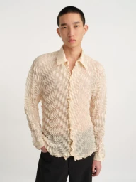 Model wearing a textured cream long-sleeve button-up shirt and dark trousers against a white seamless background