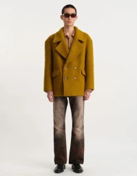 Model wearing a textured mustard yellow double-breasted coat and gradient trousers against a clean white background