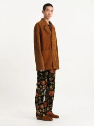 Model wearing brown textured coat and floral patterned trousers against white background