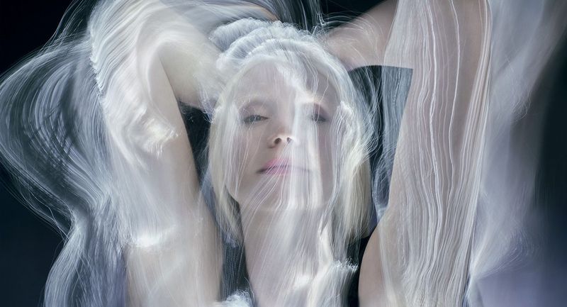 Portrait of an adult female with her hands behind her head, captured in a studio with long exposure motion blur photography.