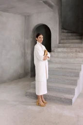 Model Marimar Cardenas posing in an ivory coat, matching skirt, and yellow platform sandals beside concrete steps.