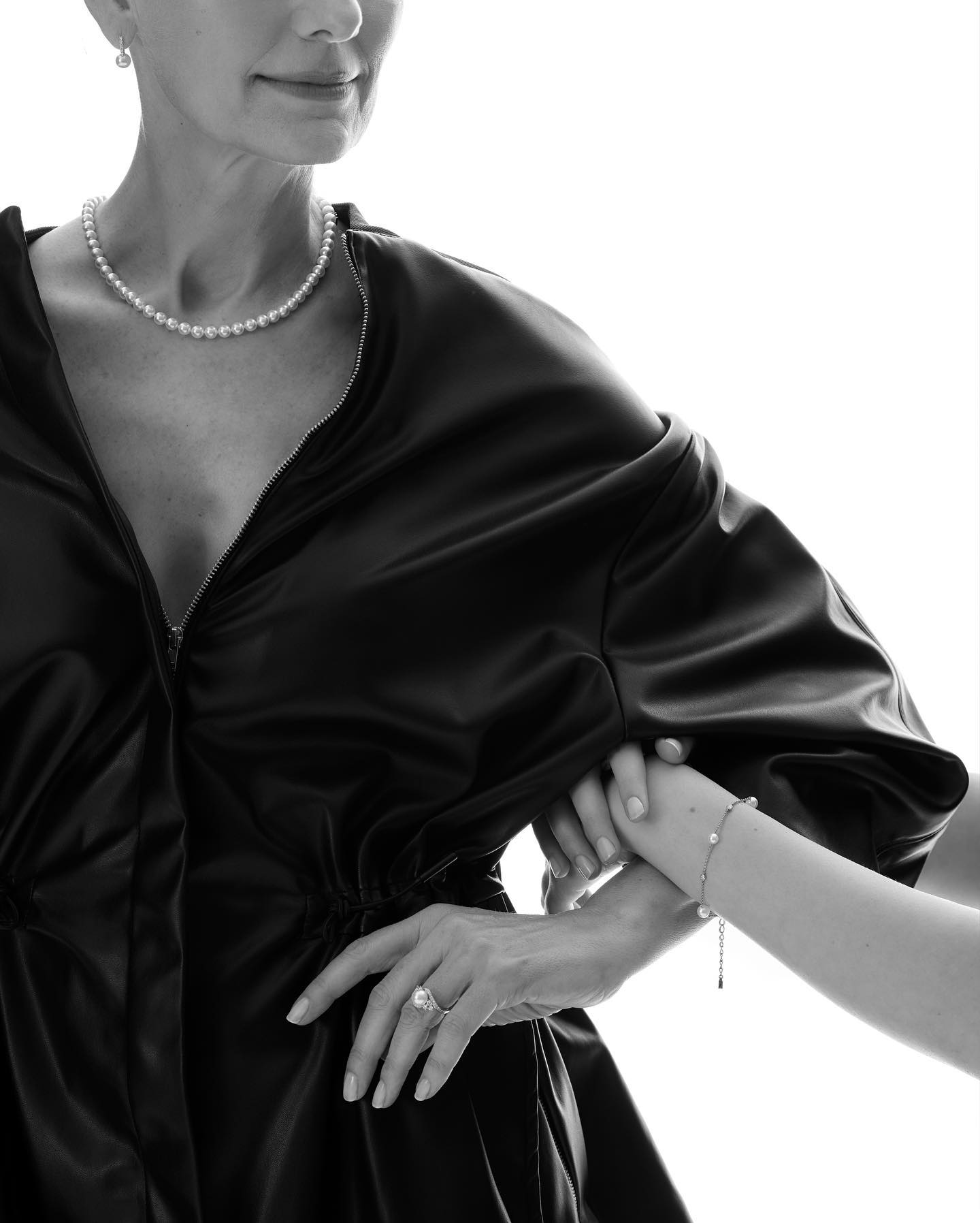 Black and white portrait of a mature woman with pearl jewelry, holding hands with a child. Fashion editorial against white.