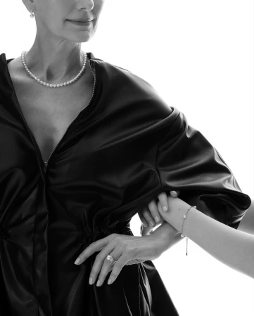 Black and white portrait of a mature woman with pearl jewelry, holding hands with a child. Fashion editorial against white.