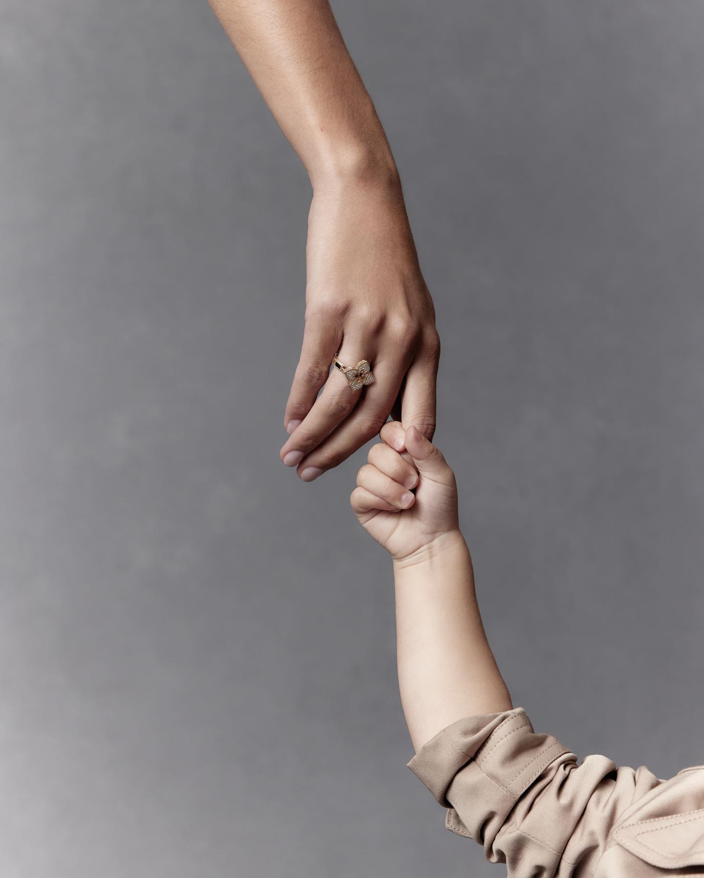 A close-up image shows an adult's hand holding a baby's fingers against a grey backdrop. A gold ring adorns the adult's hand.